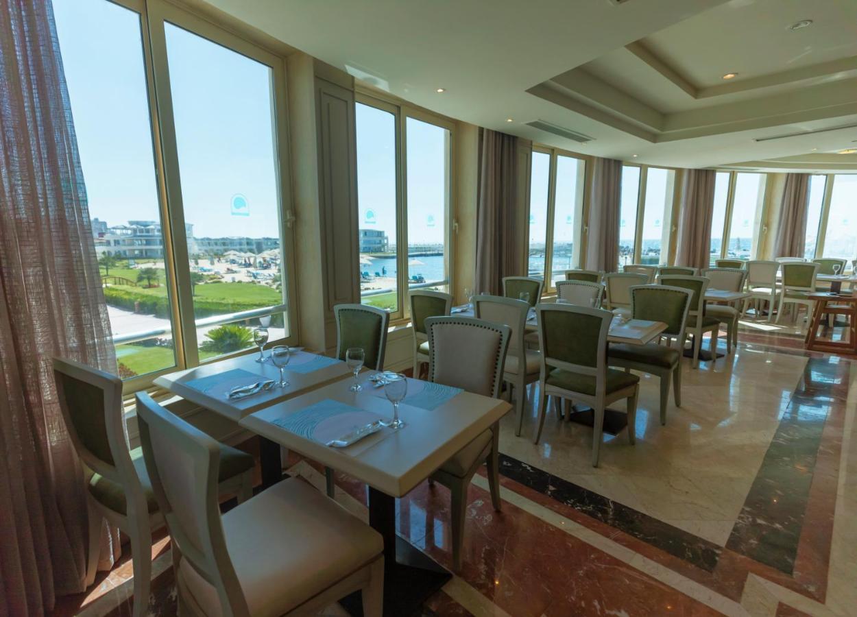 Sunrise Alex Avenue Hotel Alexandria Eksteriør bilde The photo shows an elegant restaurant interior with several tables and chairs arranged in a spacious setting. The dining area features large windows that allow natural light to flood in, offering a view of the outdoor landscape. The tables are set wi