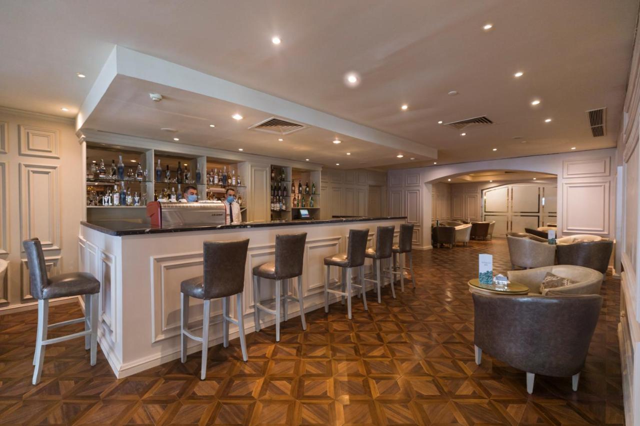 Sunrise Alex Avenue Hotel Alexandria Eksteriør bilde The photo shows a modern bar area with a sleek, minimalist design. The bar itself features a long countertop with several high-backed chairs positioned in front of it. Behind the bar, shelves are lined with various bottles of alcoholic beverages. The