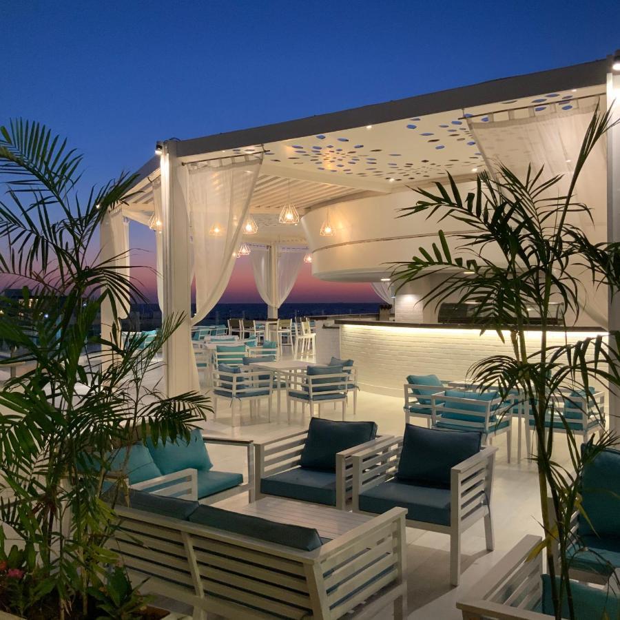 Sunrise Alex Avenue Hotel Alexandria Eksteriør bilde The photo shows a stylish outdoor terrace or rooftop lounge area. It features white furniture, including comfortable seating with teal cushions. The space is adorned with draped sheer curtains, providing a relaxed and elegant atmosphere. Lush green p