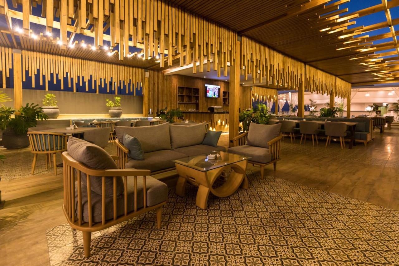 Sunrise Alex Avenue Hotel Alexandria Eksteriør bilde The photo depicts a stylish and modern lounge or restaurant interior. It features wooden furniture, including a sofa and armchairs, arranged around a central coffee table. The space is characterized by warm lighting and decorative elements, such as h