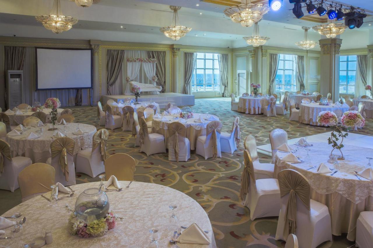 Sunrise Alex Avenue Hotel Alexandria Eksteriør bilde The photo shows an elegantly designed banquet hall set up for an event. There are several round tables covered with light-colored tablecloths, each adorned with decorative centerpieces, such as floral arrangements. The chairs are draped with fabric t