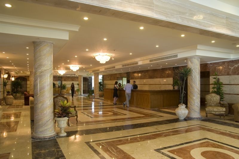 Sunrise Alex Avenue Hotel Alexandria Eksteriør bilde The photo shows the interior of a spacious lobby, likely in a hotel. There are marble floors with intricate patterns, elegant lighting fixtures, and tall pillars. In the center, there is a reception desk where staff members are attending to guests. S