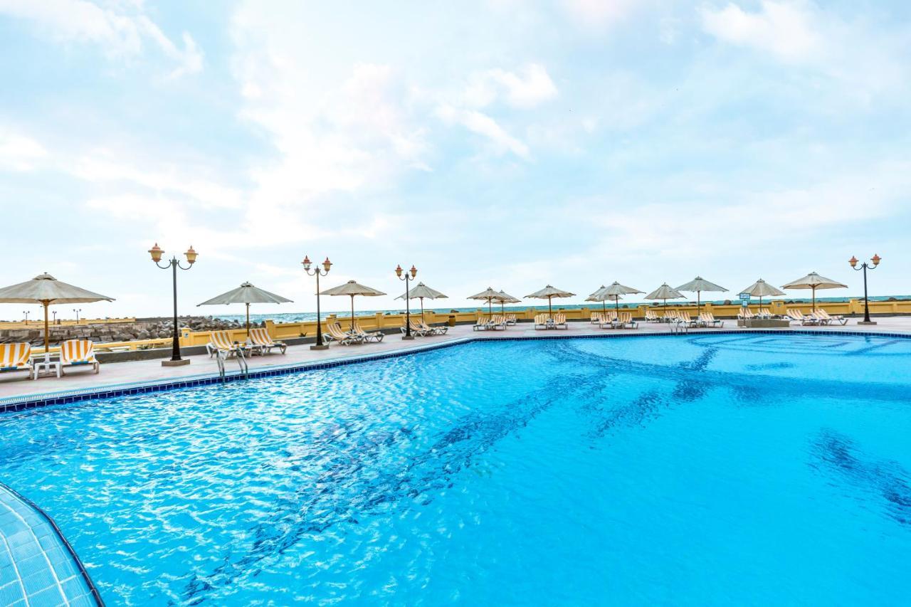 Sunrise Alex Avenue Hotel Alexandria Eksteriør bilde The photo shows a large swimming pool with crystal clear blue water. Surrounding the pool are several sun loungers and umbrellas, providing shade for relaxation. In the background, there appear to be more lounge chairs and additional umbrellas, sugge